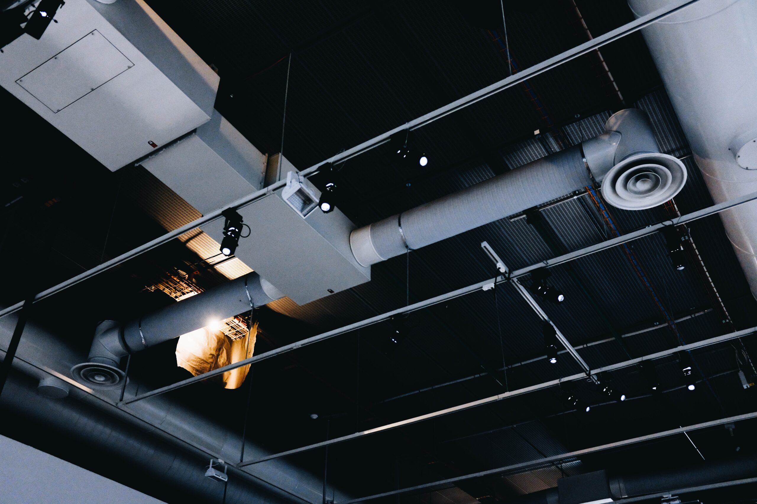 A low angle shot of a metal black ceiling with white ventilation pipes